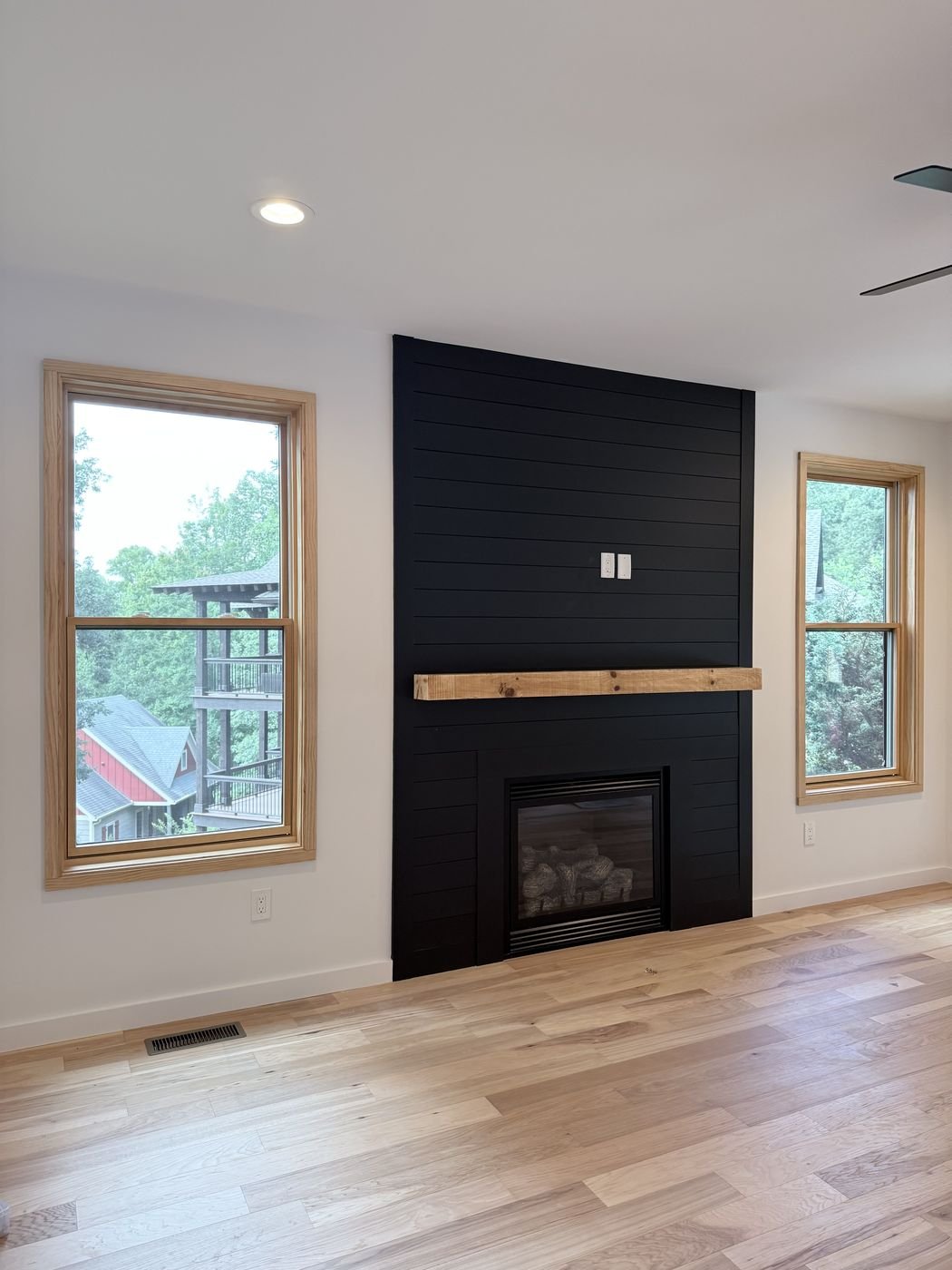 Floating wood mantel on a modern black shiplap fireplace surround