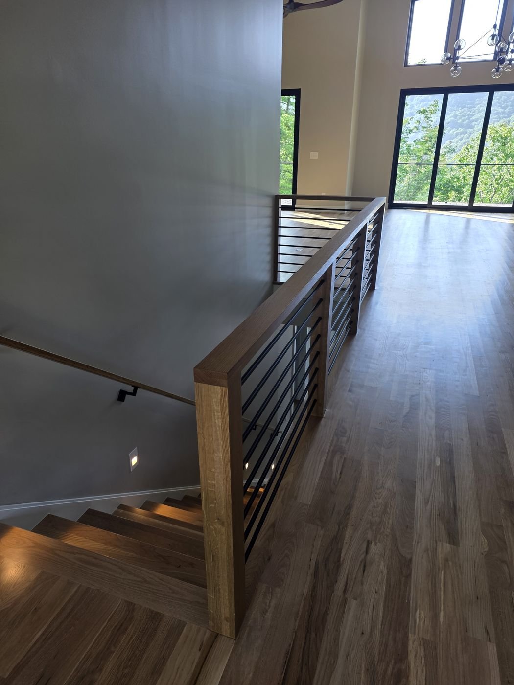 Modern wood and metal stair railing overlooking an open hardwood landing